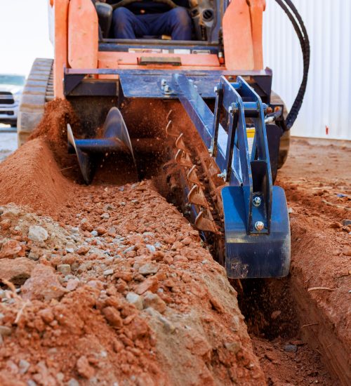 Worker operates trencher to dig trench in ground for construction purposes