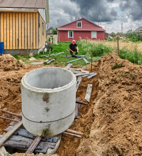 When installing next concrete ring for septic tank, builder slows its descent along roller flooring using winch.